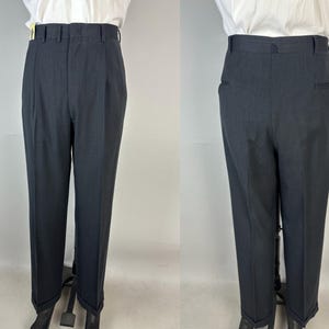 May include: A pair of charcoal gray trousers featuring a high-waisted design with a structured waistband, belt loops, and a front zipper closure. The trousers have a tailored fit with pressed creases down the front and cuffed hems at the bottom.