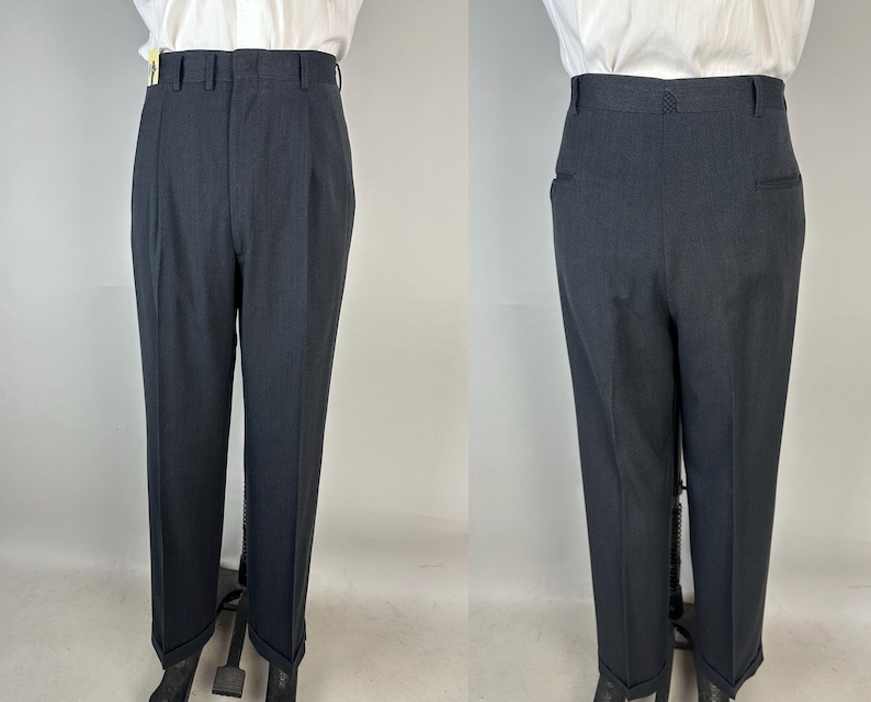 May include: A pair of charcoal gray trousers featuring a high-waisted design with a structured waistband, belt loops, and a front zipper closure. The trousers have a tailored fit with pressed creases down the front and cuffed hems at the bottom.