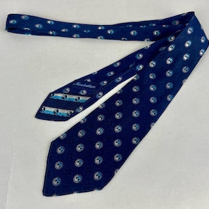 May include: A navy blue tie featuring a repeating pattern of white and light blue circles. The tie has a label that reads "Manhattan". The tie is made of a smooth fabric.