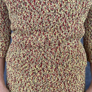 May include: A two-piece knit set in a speckled pattern of yellow, red, and brown. The top has short sleeves and a fitted waist. The skirt has a tiered design. The fabric has a textured appearance.