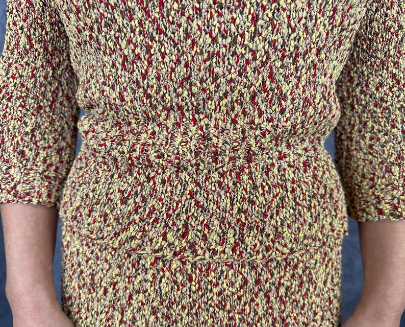 May include: A two-piece knit set in a speckled pattern of yellow, red, and brown. The top has short sleeves and a fitted waist. The skirt has a tiered design. The fabric has a textured appearance.