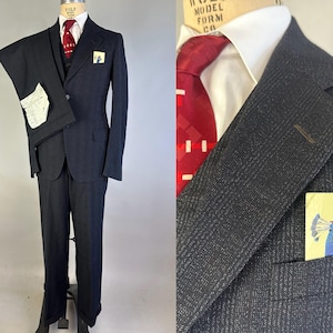 May include: A dark charcoal gray suit featuring a textured fabric, a white dress shirt, and a deep red necktie with a white geometric pattern. A pocket square displays a colorful illustration of a peacock wearing a red hat in the breast pocket.