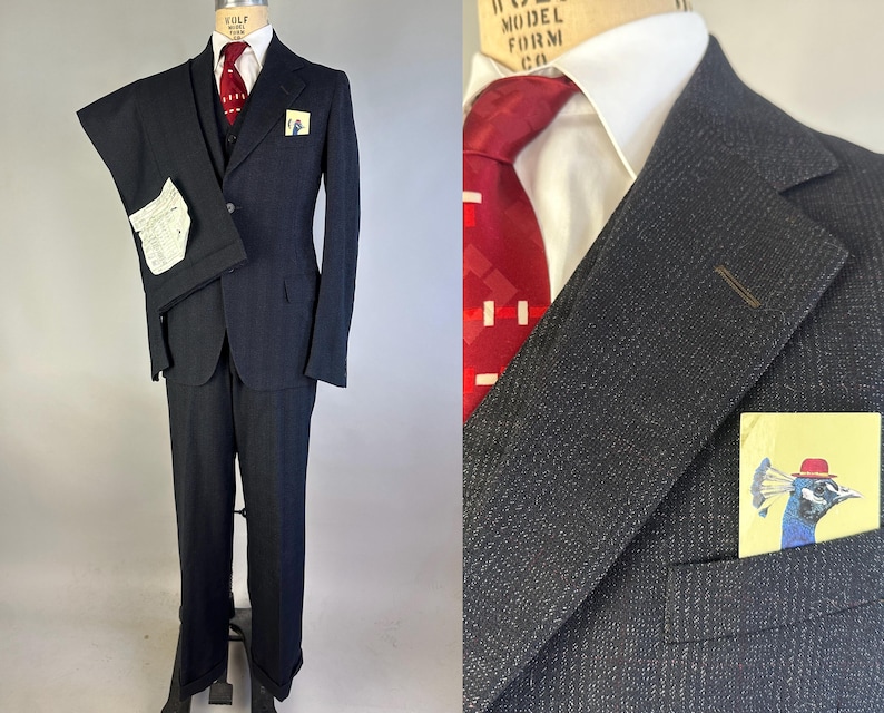 May include: A dark charcoal gray suit featuring a textured fabric, a white dress shirt, and a deep red necktie with a white geometric pattern. A pocket square displays a colorful illustration of a peacock wearing a red hat in the breast pocket.