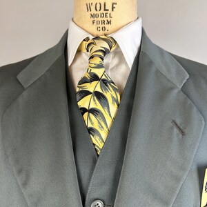 May include: A gray suit jacket with a yellow and green patterned tie and a pocket square with a peacock design. The jacket has a lapel and a button closure. The text "WOLF MODEL FORM CO." is visible on the collar.