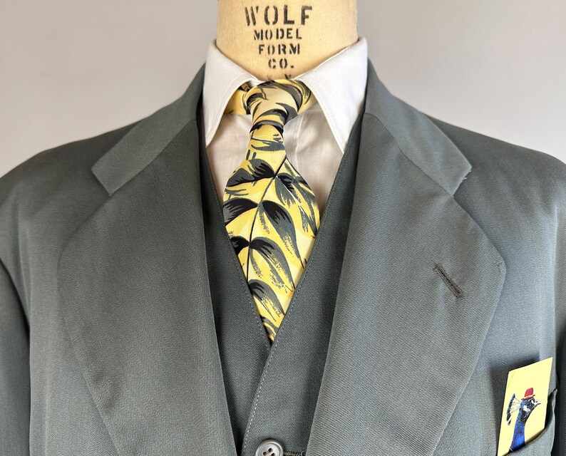 May include: A gray suit jacket with a yellow and green patterned tie and a pocket square with a peacock design. The jacket has a lapel and a button closure. The text "WOLF MODEL FORM CO." is visible on the collar.