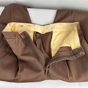 May include: Brown dress pants with a zipper fly and button closure. The pants have a classic design with a tailored fit. The interior lining is a light yellow color. The pants are made of a durable fabric.
