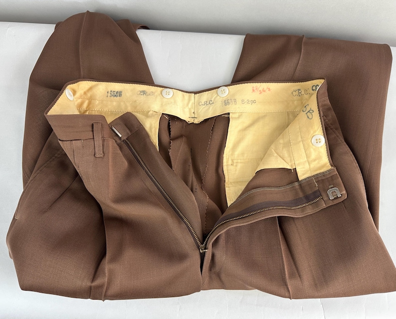 May include: Brown dress pants with a zipper fly and button closure. The pants have a classic design with a tailored fit. The interior lining is a light yellow color. The pants are made of a durable fabric.