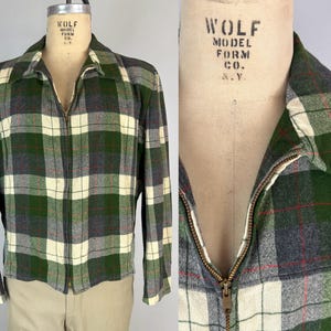 Peut inclure: Une veste à manches longues avec un motif à carreaux dans des tons de vert forêt, crème et gris anthracite, agrémentée de fines lignes rouges. La veste présente un col pointu, une fermeture éclair métallique centrale et des manches longues.