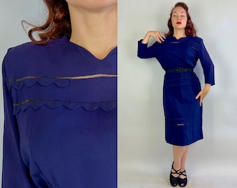 May include: A navy blue dress with a scalloped lace trim and a belt. The dress has a long sleeve and a knee-length skirt.