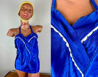 May include: A blue satin swimsuit with white trim. The swimsuit has a halter neckline and a V-shaped front.