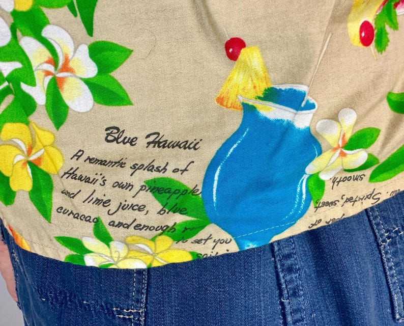May include: Tan fabric with a tropical print featuring a blue cocktail, yellow pineapple, and red cherries. The design includes white and yellow flowers with green leaves, and the text "Blue Hawaii".