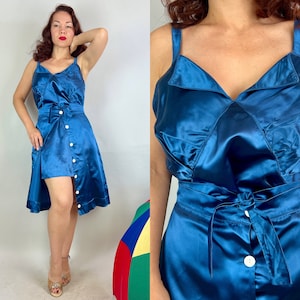 May include: A blue satin dress with a button-up front and a tie at the waist. The dress has a fitted bodice and a flowing skirt.