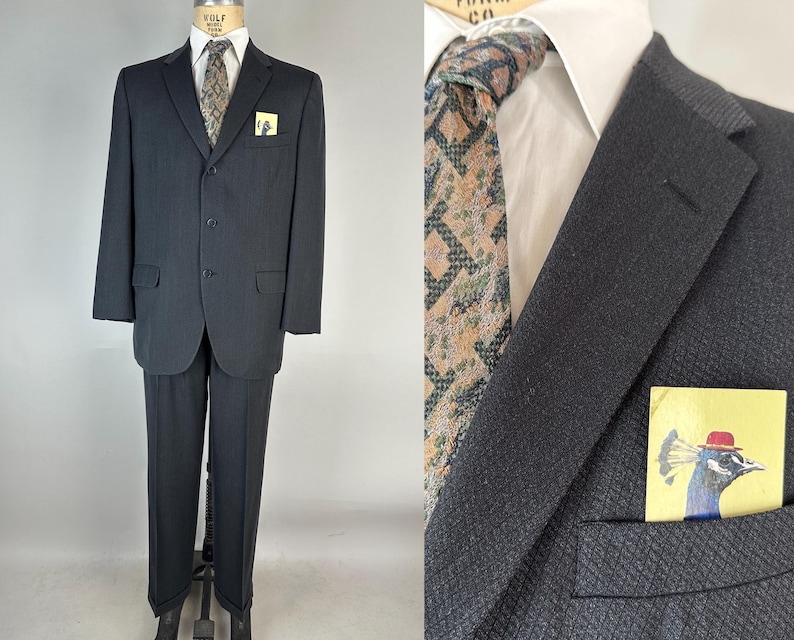 May include: A dark charcoal suit featuring a white collared shirt, a patterned tie in shades of brown and green, and a pocket square displaying a graphic illustration of a peacock wearing a red hat. The suit jacket has three buttons and flap pockets.