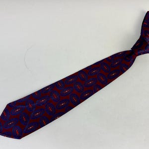 May include: A burgundy tie with a repeating paisley pattern in navy blue and red. The tie is knotted, showcasing the intricate design and color contrast. The tie is made of a smooth fabric.