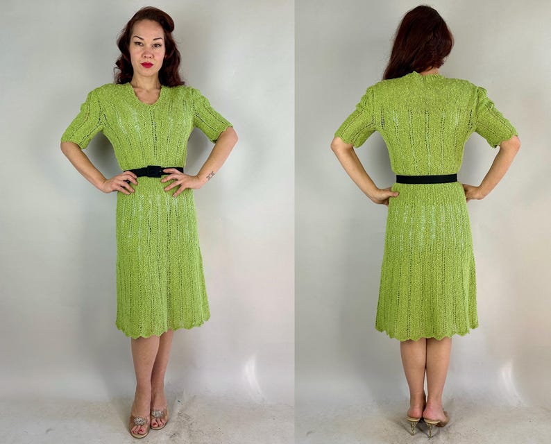 May include: A lime green knitted dress with short sleeves and a V-neck. The dress has a scalloped hemline and is cinched at the waist with a black belt. The dress is knee-length and appears to be vintage.
