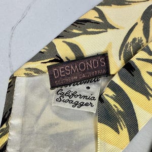 May include: A yellow and black patterned silk tie with a brown label that reads "DESMOND'S SOUTHERN CALIFORNIA California Swagger".