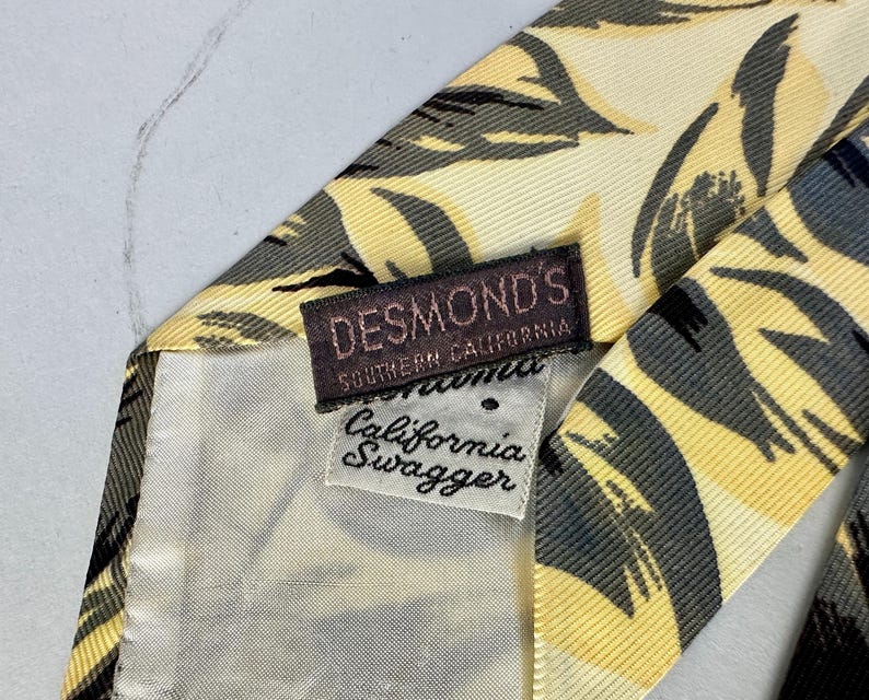 May include: A yellow and black patterned silk tie with a brown label that reads "DESMOND'S SOUTHERN CALIFORNIA California Swagger".