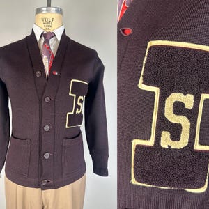 以下が含まれることがあります： 左袖に大きなフェルトの文字「S」が付いた、マルーン色のカーディガン。カーディガンはVネック、ポケットが2つ、フロントにボタンが5つ付いています。