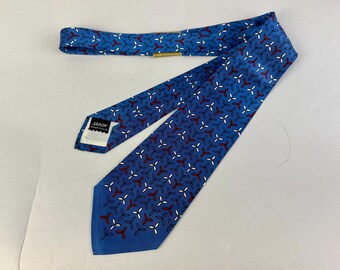 May include: A blue necktie featuring a repeating pattern of small, three-petaled floral shapes in white and red. The tie includes a black and white label on the back that reads Arrow, with a small gold-toned metal clip attached to the fabric.