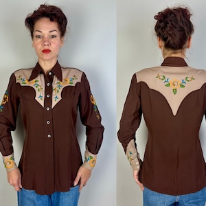 May include: A long-sleeved button-down shirt in dark brown featuring a tan yoke and cuffs. The shirt is decorated with embroidered floral patterns in yellow, blue, and green on the front yoke, sleeves, cuffs, and the back yoke area.