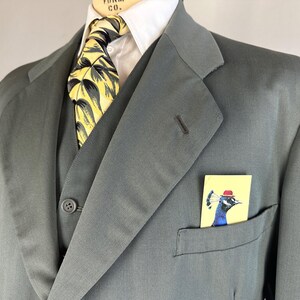 May include: A dark gray suit jacket with a yellow and black patterned tie and a pocket square featuring a peacock wearing a red hat.