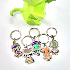 May include: A selection of character keyrings with vibrant designs. The keyrings have silver rings and feature different characters. A geometric lime green cat sculpture is in the background.