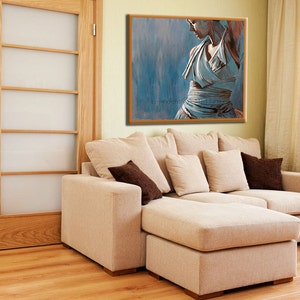 May include: A beige sectional sofa with a chaise lounge, featuring a brown throw pillow and several white pillows. The sofa is positioned in front of a wall with a framed painting of a woman in a blue dress.