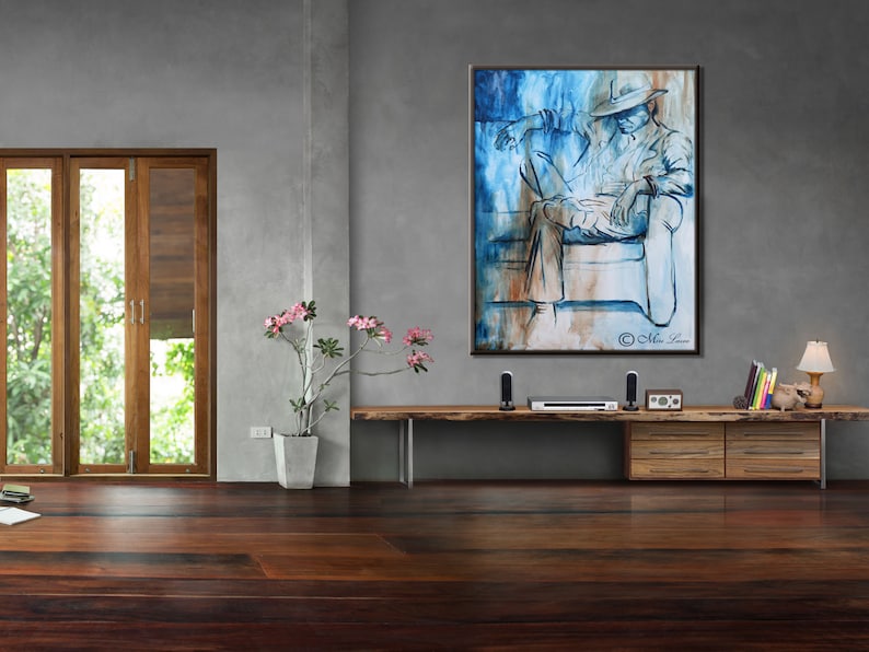 Puede incluir: Una pintura abstracta azul y marr&oacute;n de una persona sentada en un sof&aacute;. La pintura est&aacute; enmarcada y colgada en una pared gris.