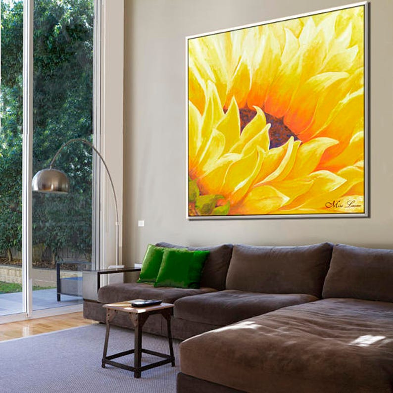 May include: A large, close-up painting of a sunflower with yellow petals and a dark brown center. The painting is framed and hanging on a wall in a living room.