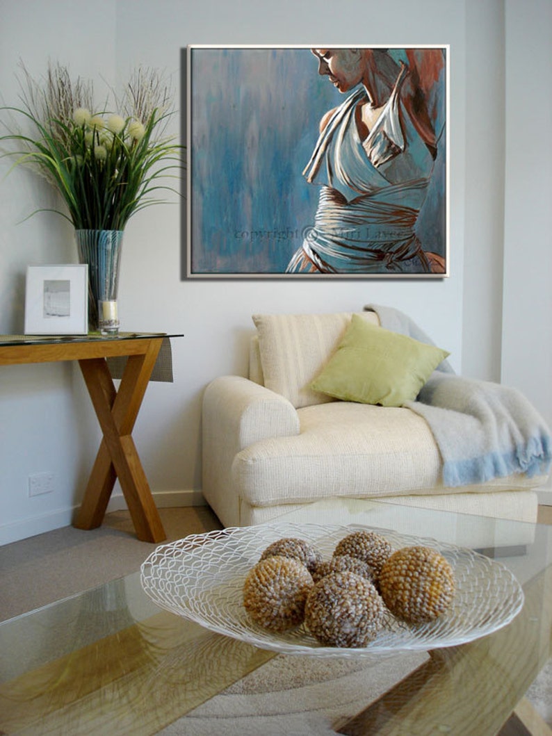 May include: A white couch with a green pillow and a blue throw blanket. A glass coffee table with a white wire bowl filled with decorative balls. A painting of a woman in a white dress hangs on the wall above the couch. The painting has a blue background with a light pink and gray overlay. The text "Copyright Muri Laws" is visible in the bottom right corner of the painting.