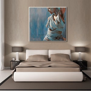 May include: A painting of a woman in a white dress, standing in a blue and gray background. The painting is framed in a white frame and is hanging on a wall above a bed.