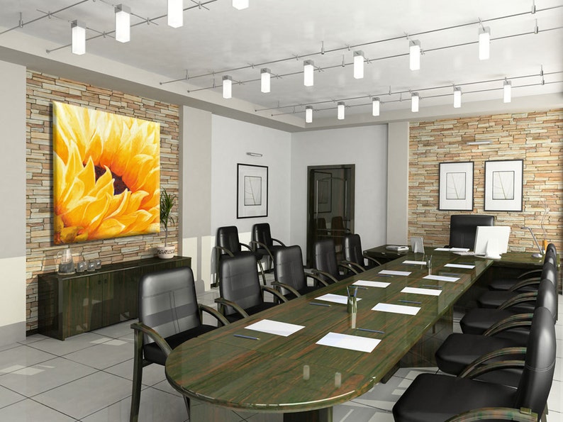 May include: A modern conference room with a large sunflower painting on the wall, a long wooden table with black chairs, and a stone wall with framed artwork.