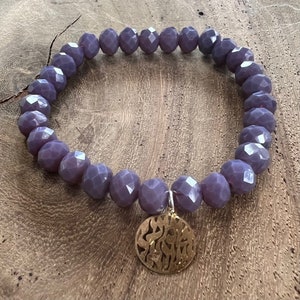 May include: A purple beaded bracelet with a gold charm. The charm has a decorative design.
