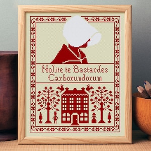 Puede incluir: Patrón de punto de cruz con una figura vestida de rojo con una capucha blanca, una casa con ventanas y árboles. El texto "Nolite te Bastardes Carborundorum" se muestra debajo de la figura.