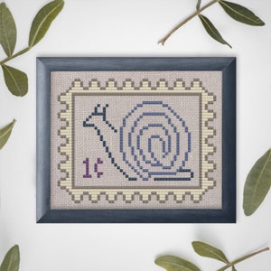 May include: A framed cross-stitch design of a snail with a shell in a spiral shape. The snail is on a beige background with a brown border and the text "1¢" in purple.
