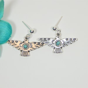 May include: A pair of silver earrings with turquoise stones. Each earring features a stylized bird design with intricate details.