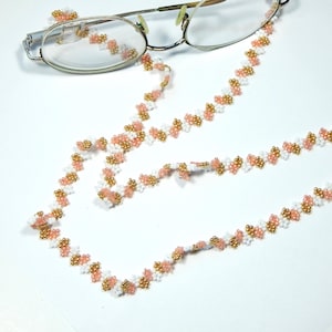 May include: A beaded eyeglass chain and matching ear pieces. The chain is made of white, gold, and pink beads. The glasses are silver-framed. The chain is designed to be worn around the neck to hold eyeglasses.