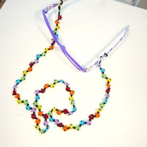May include: A rainbow-colored beaded eyeglass chain with black beads and crystal-like beads. The chain is attached to a pair of purple eyeglasses.