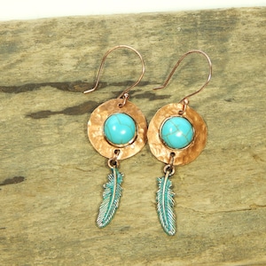 May include: A pair of copper earrings with turquoise stones and feather charms. The earrings have a hammered finish and are suspended from a hook.