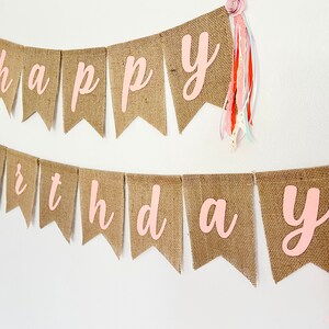 May include: A burlap banner with the words "happy birthday" in pink letters. The banner is decorated with pink and white fabric tassels.