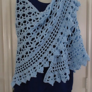 May include: A light blue crocheted shawl with a delicate openwork pattern. The shawl is draped over a mannequin wearing a blue dress.