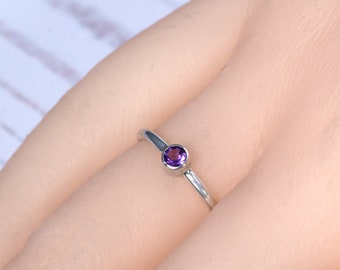 May include: A simple silver ring with a small, round, purple amethyst gemstone.
