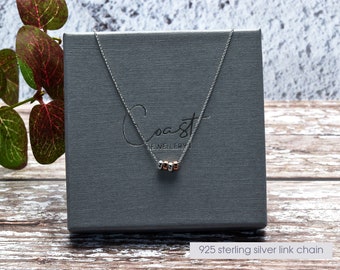 May include: A silver necklace with a silver chain and four small silver and rose gold beads. The necklace is in a gray box with the word "Coast Jewellery" printed on it. 925 sterling silver link chain.