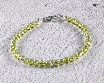 May include: A delicate bracelet featuring small, round, light green beads strung together. The bracelet has silver-colored metal accents and a clasp. The beads are evenly spaced, creating a simple yet elegant design.