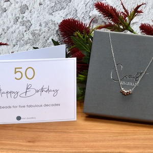 Coast Jewellery - 50th Birthday Necklace - Sterling Silver- A white card with gold lettering that reads "50 Happy Birthday" and "Five beads for five fabulous decades".