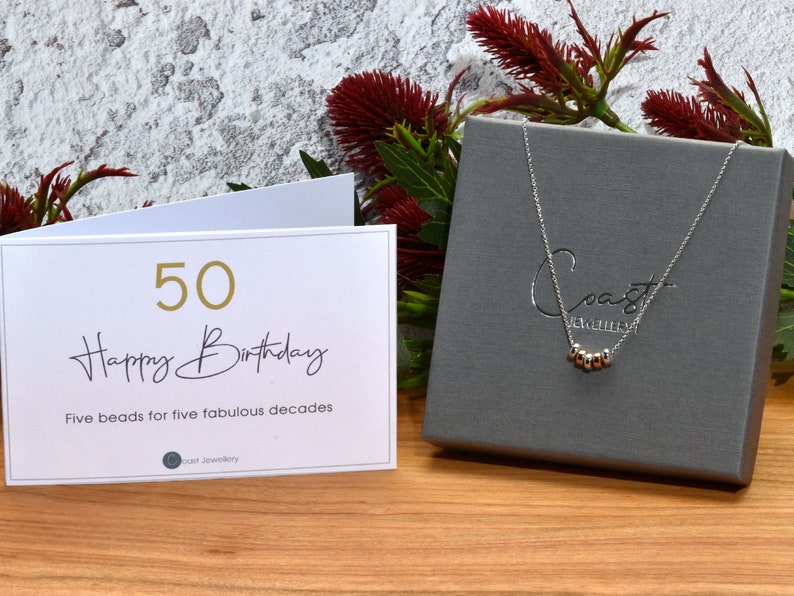 Coast Jewellery - 50th Birthday Necklace - Sterling Silver- A white card with gold lettering that reads "50 Happy Birthday" and "Five beads for five fabulous decades".