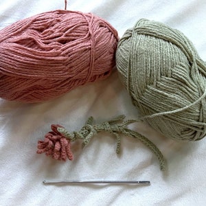 May include: Two balls of yarn, one pink and one green, with a crocheted flower and a crochet hook.