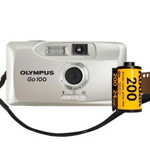 Könnte beinhalten: Eine silberne Olympus Go 100 Kamera mit schwarzem Riemen und einer Rolle Kodak 200 Farbfilm. Die Kamera hat ein Objektiv und einen Blitz. Der Film ist gelb und schwarz.