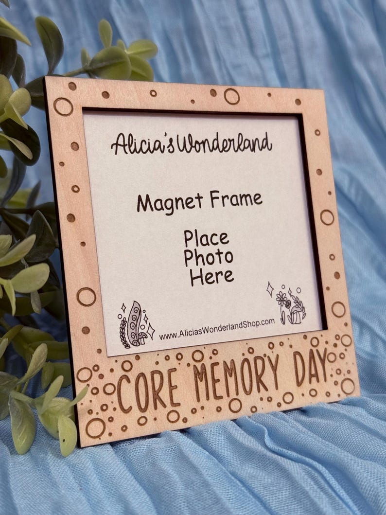 May include: A wooden magnet frame with the text "Alicia's Wonderland", "Magnet Frame", and "Core Memory Day". The frame has a rectangular opening for a photo and decorative circles.
