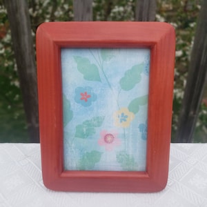 May include: A red picture frame with a floral design on the inside. The flowers are blue, yellow, and pink.